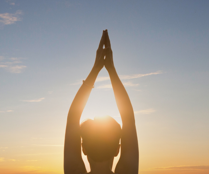 a woman reaching her arms up into the sky at sunrise in a yoga suriya namaskar pose