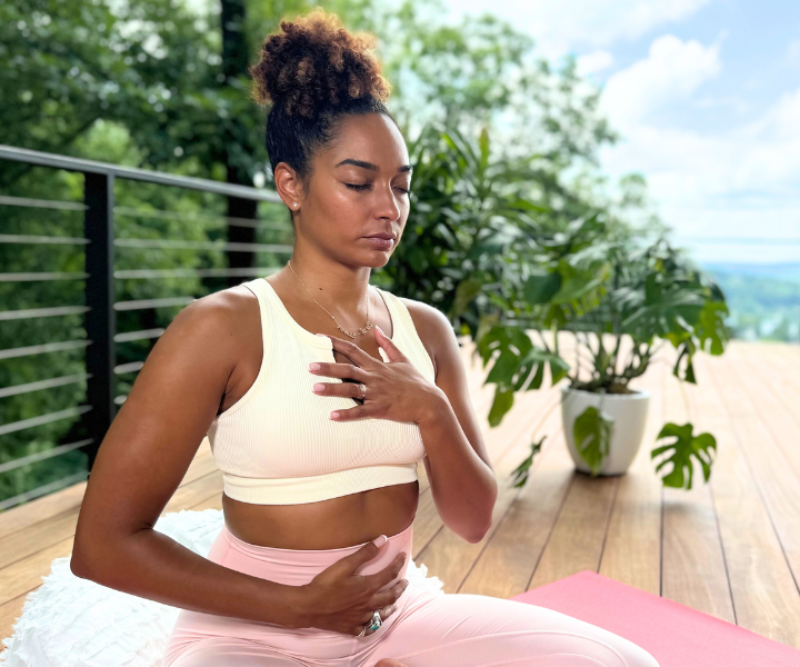 A woman with hands on chest and stomach breathing on a yoga mat in nature