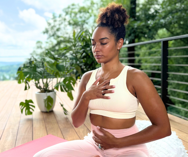 A woman with hands on chest and stomach breathing on a yoga mat in nature