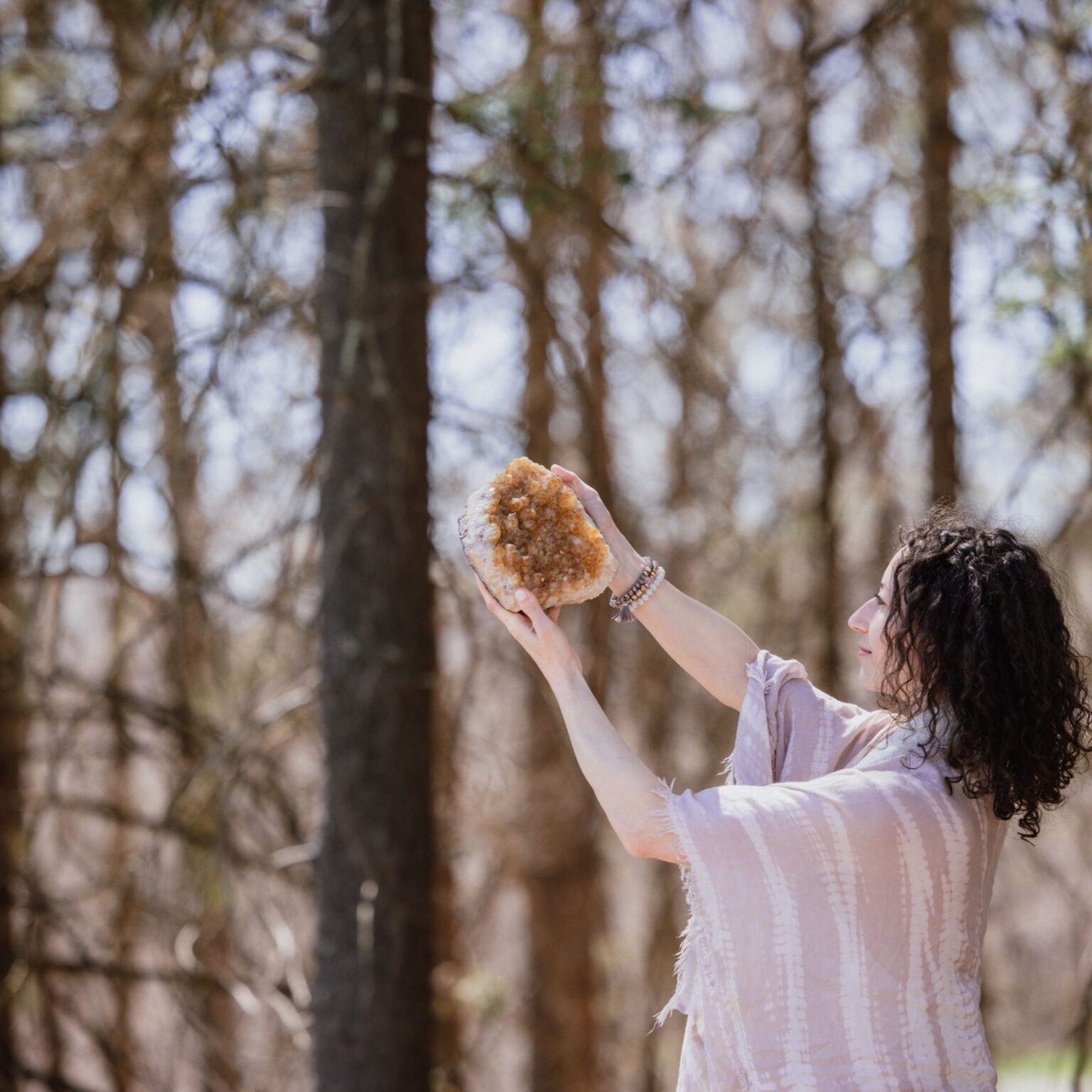 A person holds a large, amber-colored crystal geode up toward the light in a wooded area.
